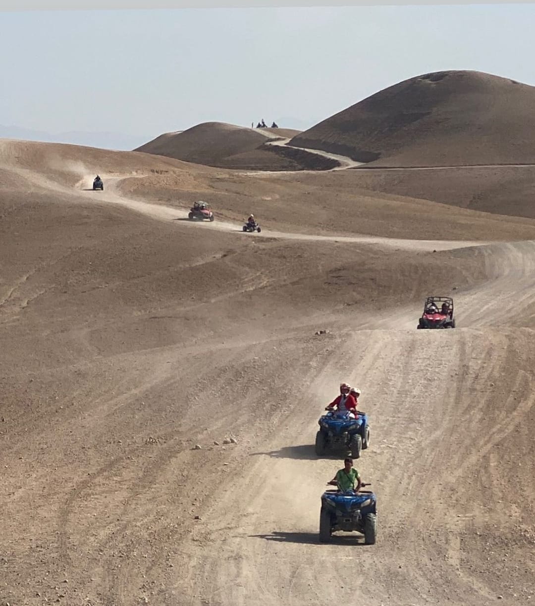 Un quad rouge conduit dans le désert d'Agafay à Marrakech, avec des montagnes en arrière-plan.